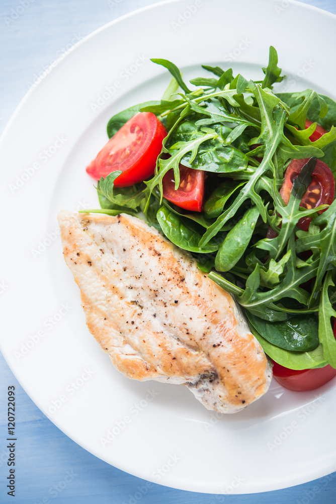 Roasted chicken breast and fresh salad with tomato and greens (spinach, arugula) top view on blue wooden background. Healthy food. Roasted chicken breast and fresh salad with tomato and greens (spinach, arugula) top view on blue wooden background. Healthy food.