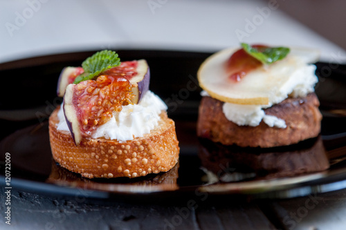 Bruschetta with goat cheese, pear and figs on black plate