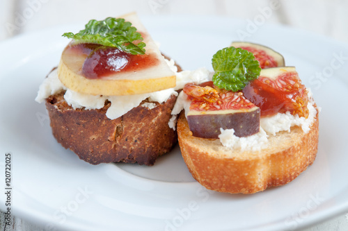 Bruschetta with goat cheese, pear and figs on white plate