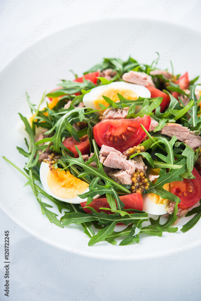 Fresh salad with tuna, tomatoes, eggs, arugula and mustard on white textured background close up. Healthy food. Fresh salad with tuna, tomatoes, eggs, arugula and mustard on white textured background close up. Healthy food.