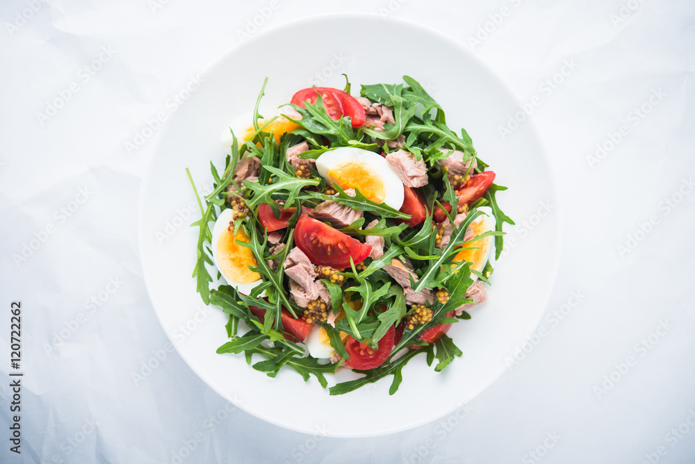 Fresh salad with tuna, tomatoes, eggs, arugula and mustard on white textured background top view. Healthy food. Fresh salad with tuna, tomatoes, eggs, arugula and mustard on white textured background top view. Healthy food.