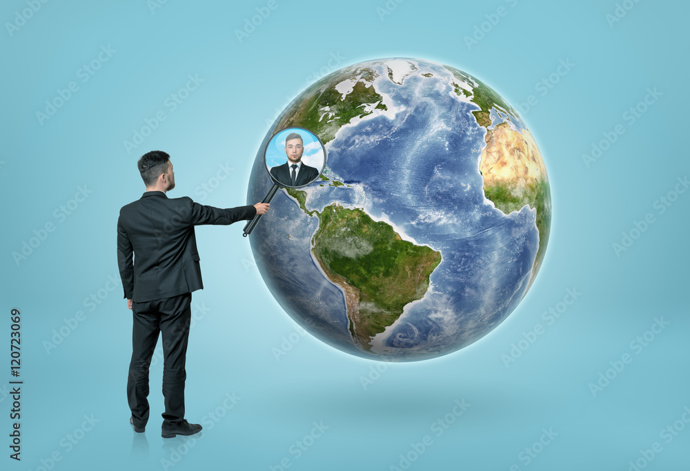 Businessman looking through magnifying glass on Earth Businessman looking through magnifying glass on Earth