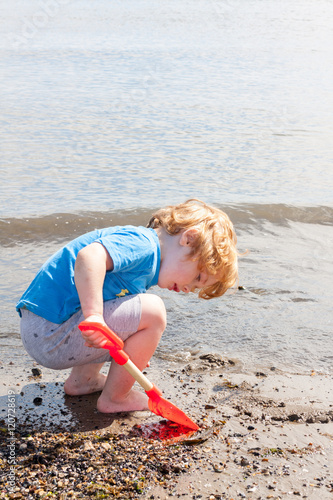 Young caucasian boy with spade playing on beach