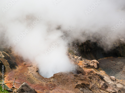 Toned image erupting water and steam geysers in the Geyser Valley at the bottom against the backdrop of huge volcano on Kamchatka peninsula in Russia