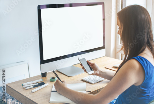 Mock-up of blank screen computer, Close up of young businesswoman looking at smartphone, Businesswoman working at modern office and using computer with blank screen, Workplace, Shallow DOF.