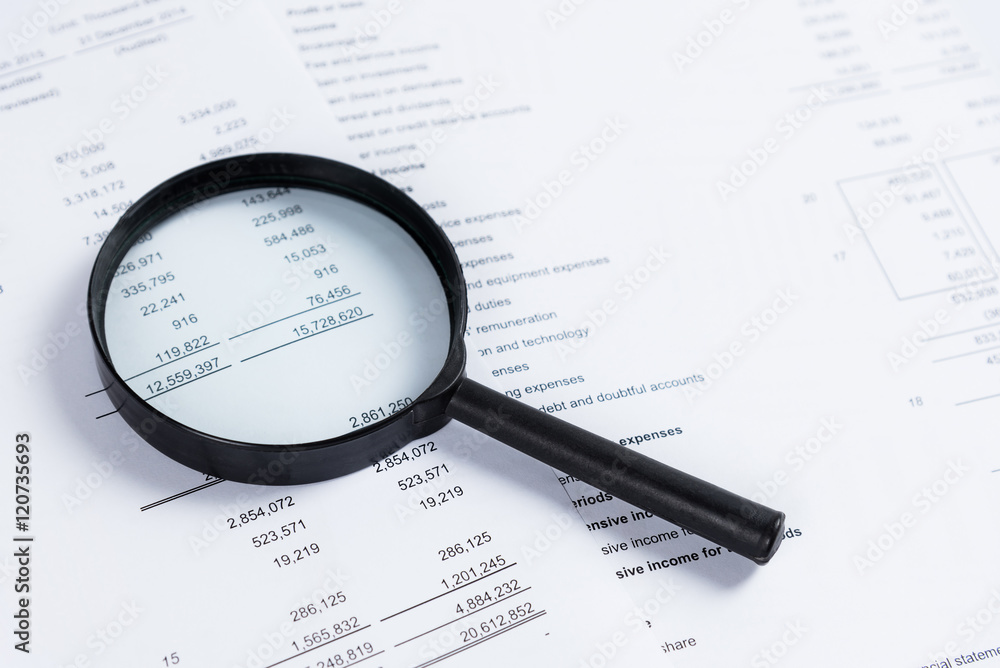 Magnifying glass on financial statement paper. Analyzing business financial data. Magnifying glass on financial statement paper. Analyzing business financial data.