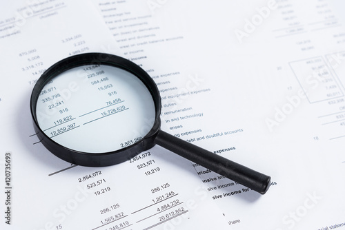 Magnifying glass on financial statement paper. Analyzing business financial data.