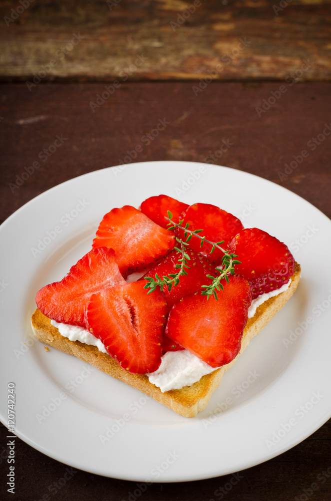 Toasted bread with cream cheese, strawberries and thyme on wooden table Toasted bread with cream cheese, strawberries and thyme on wooden table