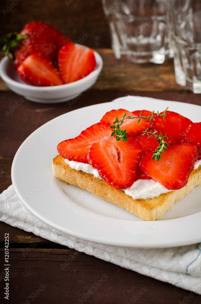 Toasted bread with cream cheese, strawberries and thyme on wooden table Toasted bread with cream cheese, strawberries and thyme on wooden table