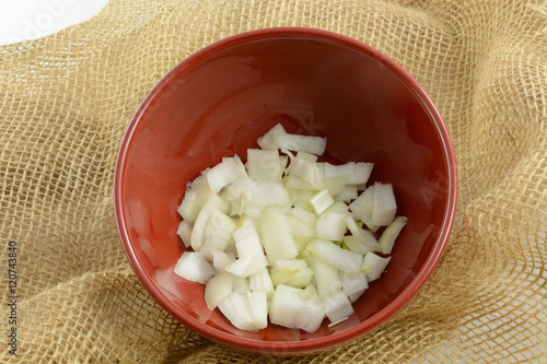 Chopped raw onions in red bowl on burlap background