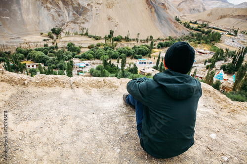 Young male traveler sitting on the sand cliff, thinking about something in Leh, Ladakh, India