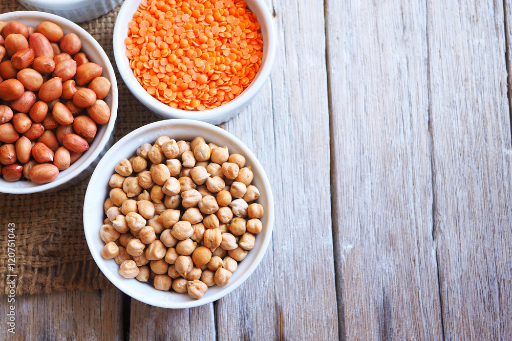 Top view of chickpeas, peanuts and red lentils on a wooden table.