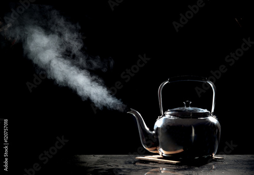 Tea kettle with boiling water on a black background photo