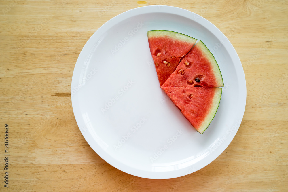 Watermelon slice on a white plate on a wood background, Top view Watermelon slice on a white plate on a wood background, Top view