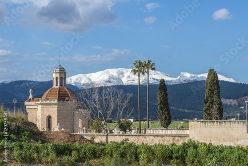 SPAIN, MALLORCA, 2015-02-07: Chapel and cemetery of Sa Pobla in front of the snow covered mountains of the Massanella range , part of the Tramuntana mountains photo