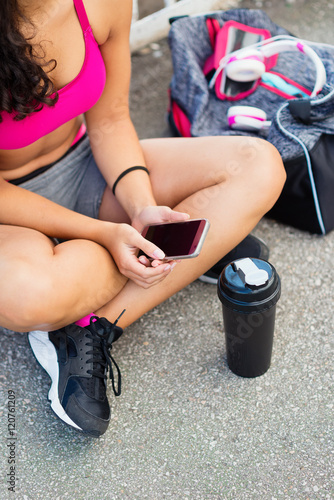 Young sporty woman t texting on smartphone after outdoor urban fitness training. Brunette girl using cellphone for messaging or internet search.