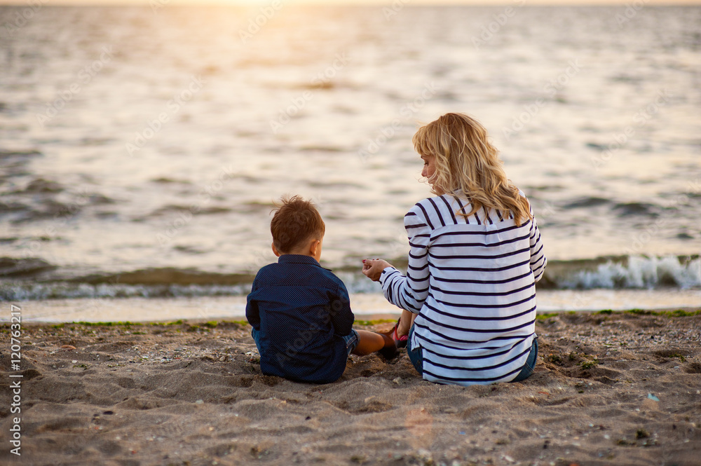 Beautiful woman with a child of four years playing on the beach near the sea Beautiful woman with a child of four years playing on the beach near the sea