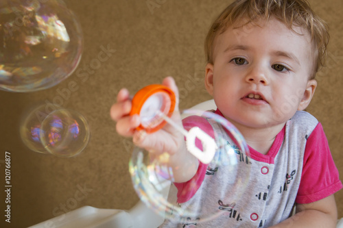 clouse-up portrait two-year girl inflates a circular bubble