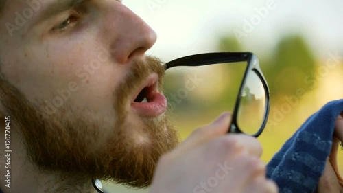Tourist wearing hat and cleaning his glasses by using tissue
