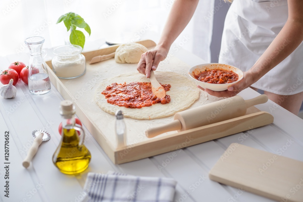 Woman adding tomato sauce on pizza