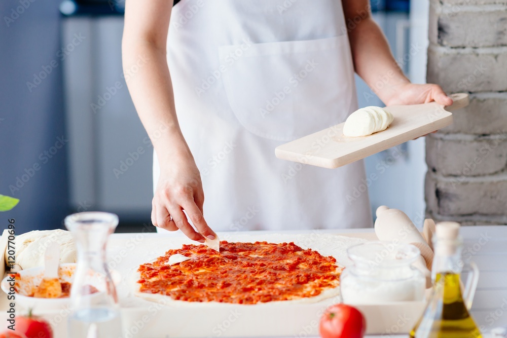 Woman puts slices of mozzarella on the pizza
