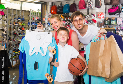man and woman with boy choosing t-shirts and other goods in spor