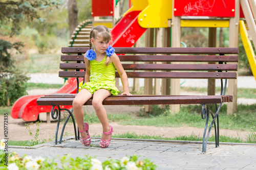Canvas Print Upset girl bit her lip while sitting on the bench on the background of the playg