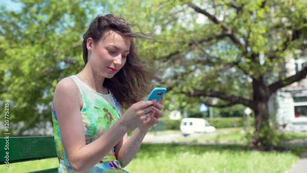 Pretty girl texting on smartphone in the park and smiling to the camera
Pretty girl texting on smartphone in the park and smiling to the camera