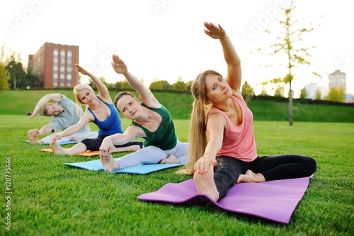 yoga group conducts training outdoors on a background of grass and sunset