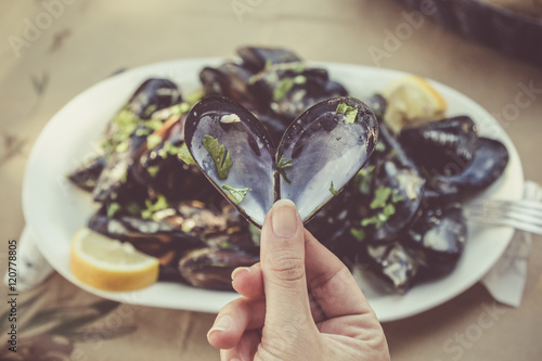 Close up of female hand holding opened heart shaped mussel at the restaurant table. Sea food and healthy eating concepts. 