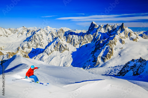 Skier skiing downhill Valle Blanche in french Alps in fresh powder snow. Snow mountain range Mont Blanc with Grand Jorasses in background.