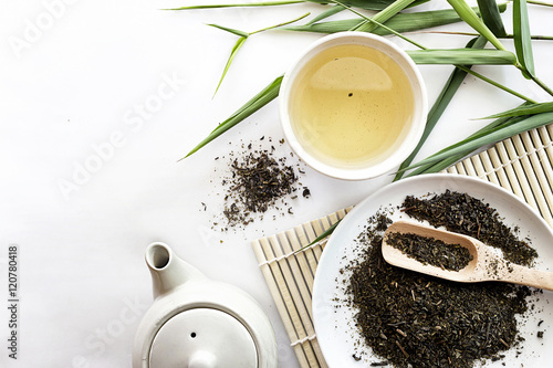teapot and cup of herbal green tea on bamboo with white table background. over light