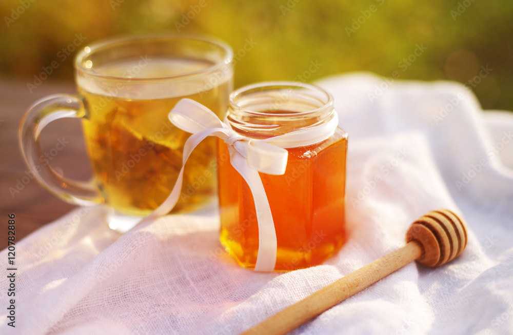 Honey in a glass jar and herbal tea in a circle on white linen fabric. Honey and tea. Soft focus Honey in a glass jar and herbal tea in a circle on white linen fabric. Honey and tea. Soft focus
