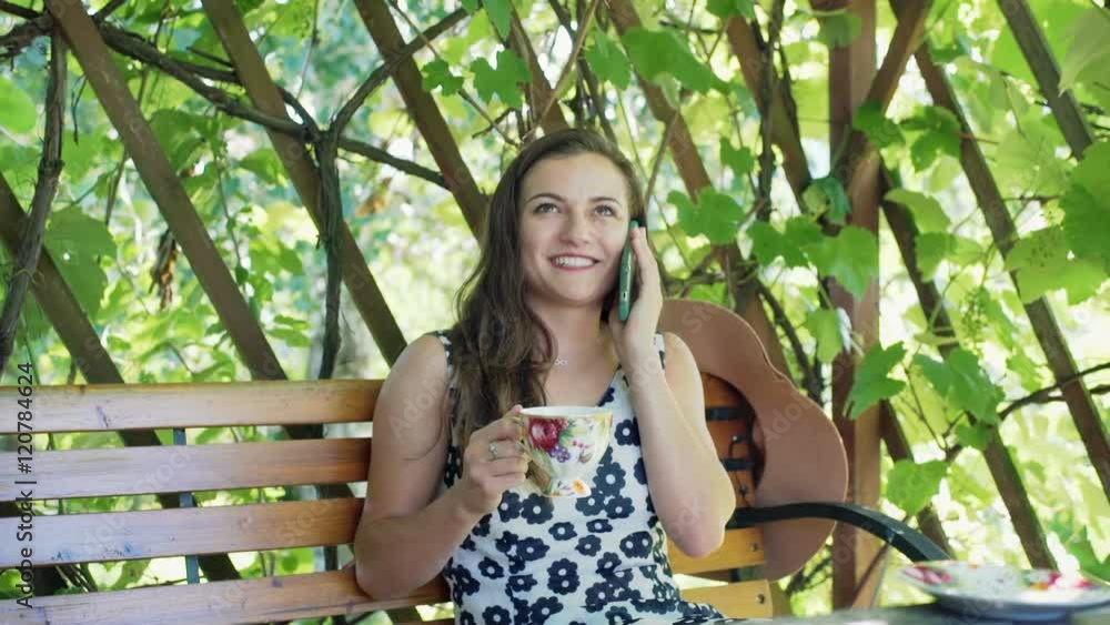 Happy girl chatting on cellphone in the arbor and holding cup of coffee
Happy girl chatting on cellphone in the arbor and holding cup of coffee