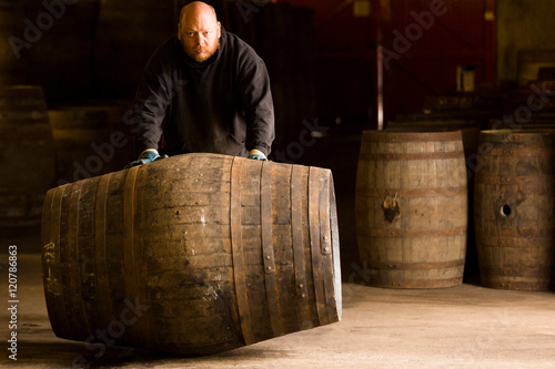 Portrait of worker rolling whisky cask in whisky distillery photo