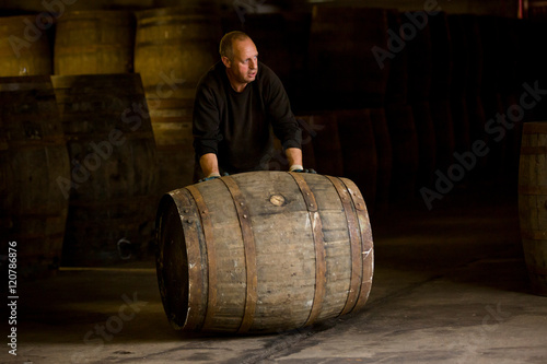 Worker rolling whisky cask in whisky distillery