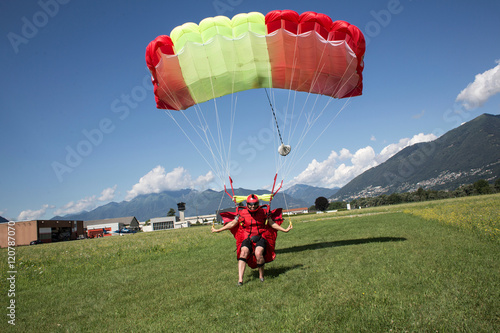 Skydiver landing parachute on field. Steering and slowing  his canopy by pulling break toggles, Locarno, Tessin, Switzerland photo