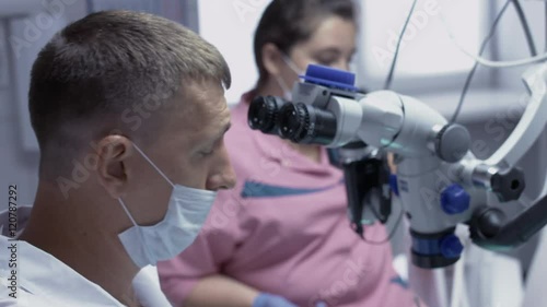 Male dentist receiving the root canals of the patient using the microscope. photo