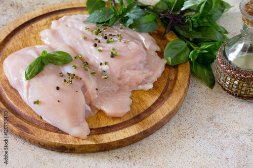 Raw chicken fillet with fresh basil on brown stone background.