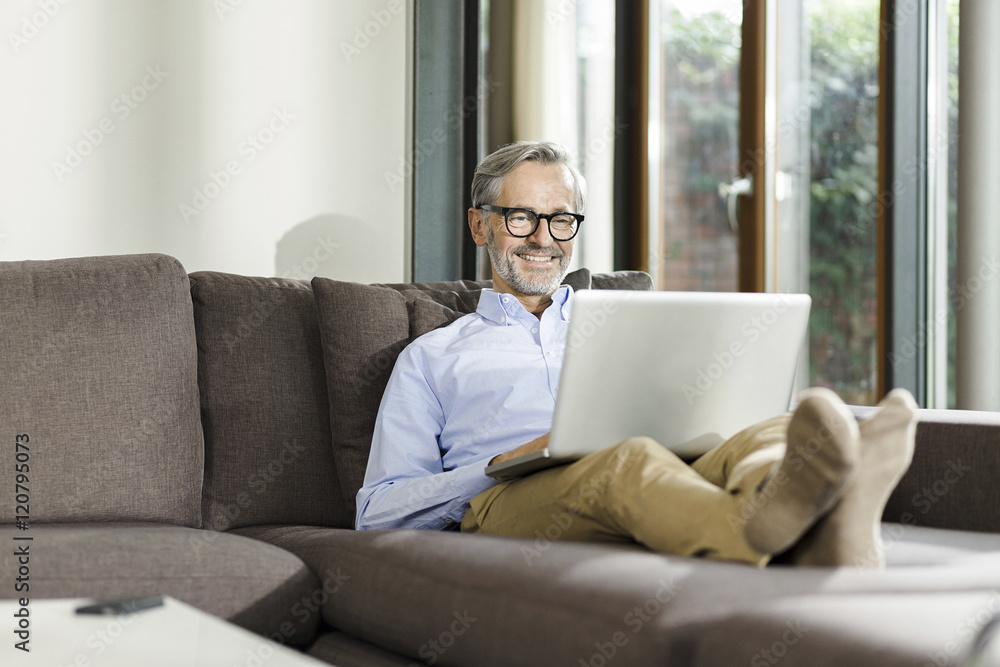Smiling man sitting on couch in his living room using laptop Smiling man sitting on couch in his living room using laptop