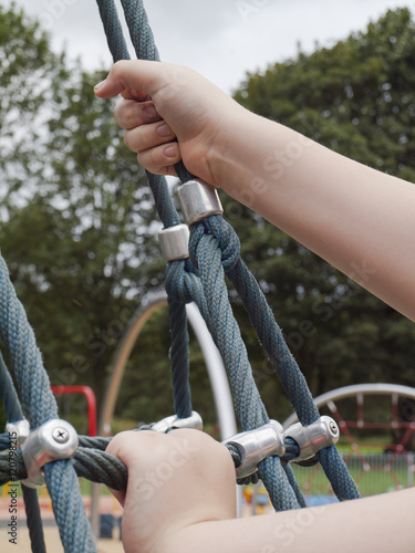 Ten year old boy reaching out ready to climb a playground scramble net.