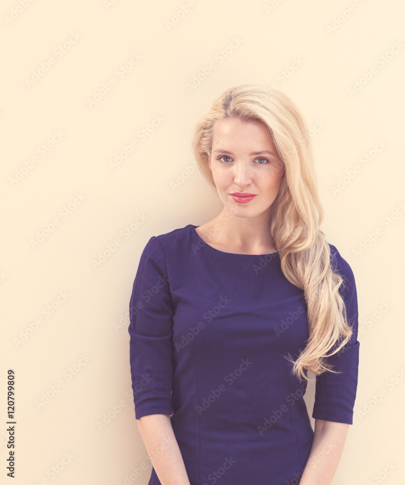 Summer portrait of young beautiful blond woman in blue dress posing near the wall. Toned in warm colors Summer portrait of young beautiful blond woman in blue dress posing near the wall. Toned in warm colors