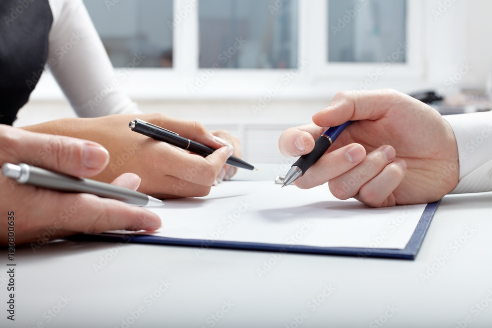 Three hands with pens over document Three hands with pens over document