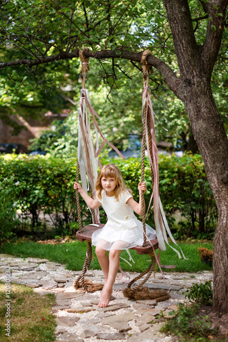 Little girl having fun on a swing outdoor. Child playing  garden playground.