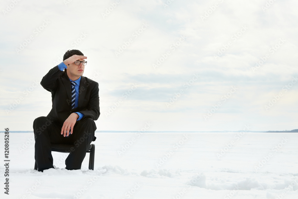 Businessman sitting on chair in snow field and looking at the horizon Businessman sitting on chair in snow field and looking at the horizon