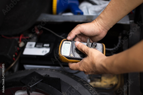 Mechanic checking a car battery level with voltmeter