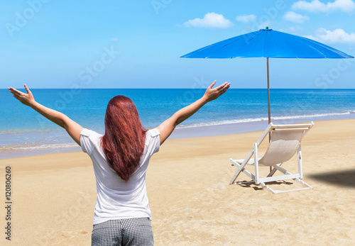 Asian woman standing raised up arms achievements celebrate successful relax on the beach with white wooden beach chair and blue parasol  background