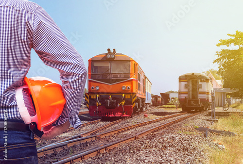 engineer holding safety helmet with orange diesel engine locomotive passenger train background