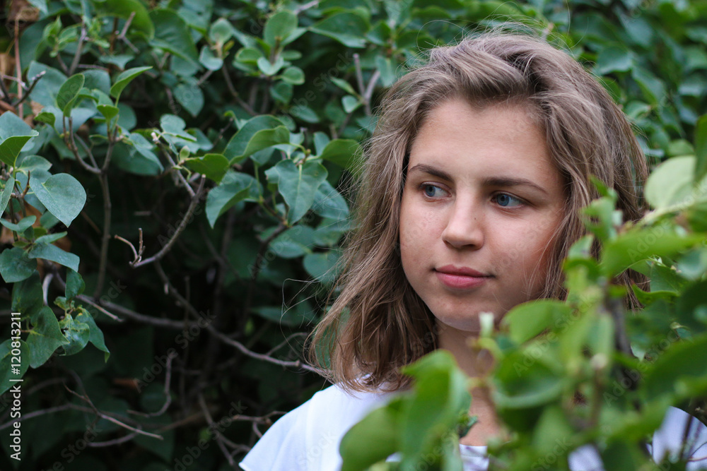 Beautiful young woman standing in the bushes and looking away Beautiful young woman standing in the bushes and looking away