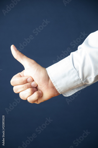 Closeup of male hand showing thumbs up sign against blue background